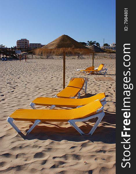 Groups of yellow beach chairs and straw umbrellas on a sandy beach - vertical