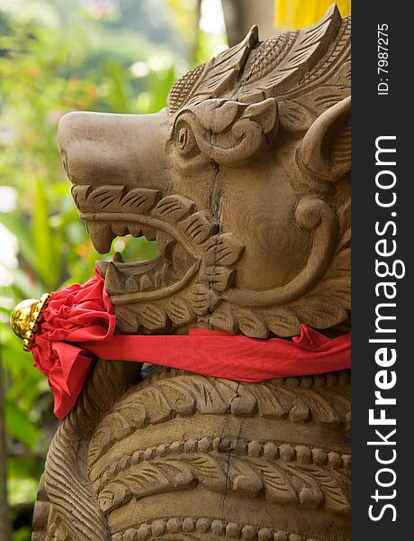 Carved wooden statue of a mythical demon guarding a door with a Chinese red bow around its neck. Carved wooden statue of a mythical demon guarding a door with a Chinese red bow around its neck