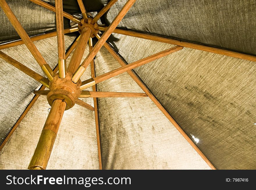 Under the canopy of a large weathered and worn garden umbrella