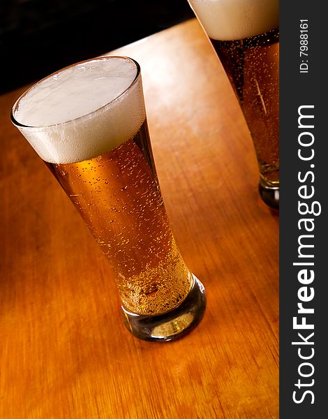 Two beer glasses on wood background, focus on first. Two beer glasses on wood background, focus on first