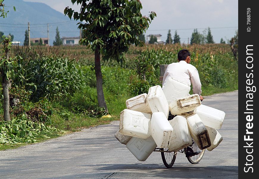 A man driving down the road with a bunch of barrels fastened to his bicycle. A man driving down the road with a bunch of barrels fastened to his bicycle