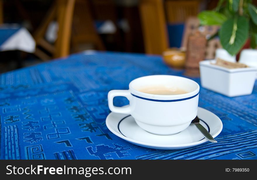 Cup of coffee on a restaurant table with blue tablecloth. Shallow depth of field with only the cup in focus.