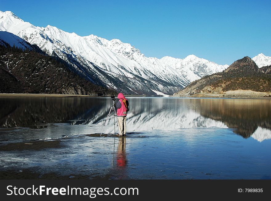 Scenery of snow mountains with their mirror and a photographer at a lake,Tibet,in a spring morning. Scenery of snow mountains with their mirror and a photographer at a lake,Tibet,in a spring morning