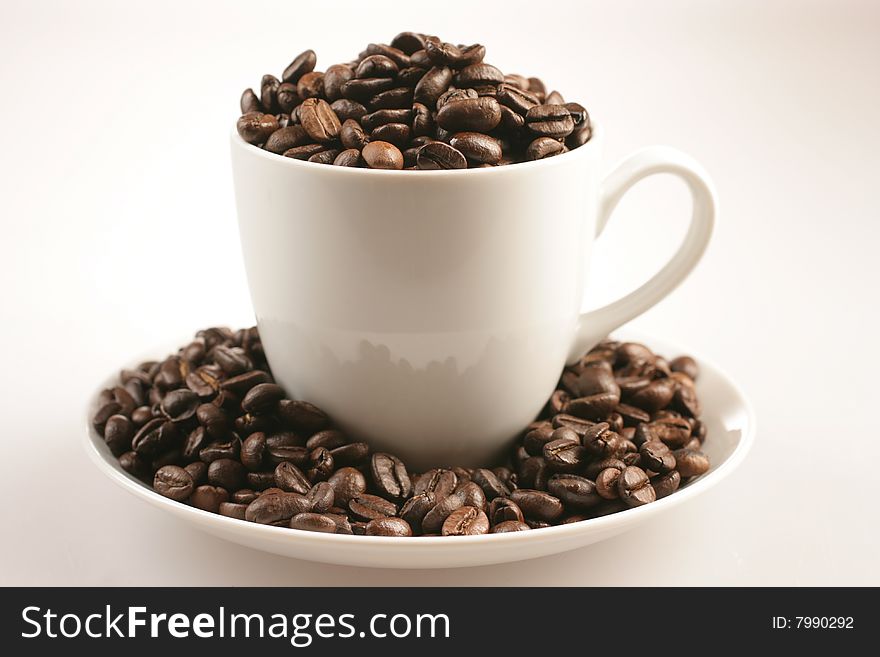 Coffee cup full of coffee beans on white plate. Coffee cup full of coffee beans on white plate