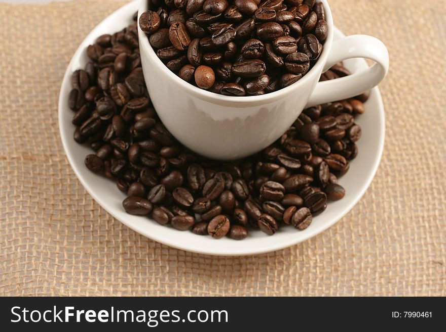 Coffee cup full of coffee beans on background of jute sack. Coffee cup full of coffee beans on background of jute sack