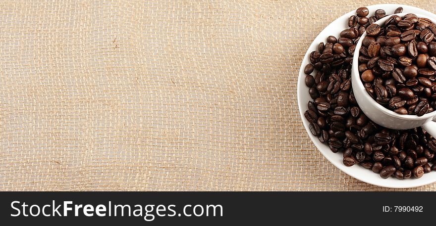 Coffee cup full of coffee beans on background of jute sack. Coffee cup full of coffee beans on background of jute sack