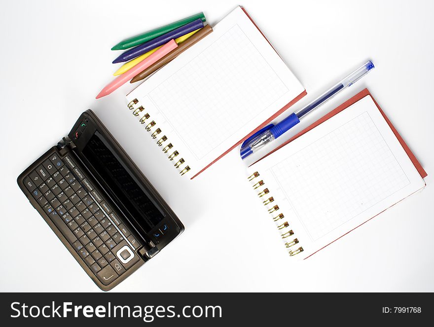 Open palmtop opposite two notebooks with pen and wax pencils