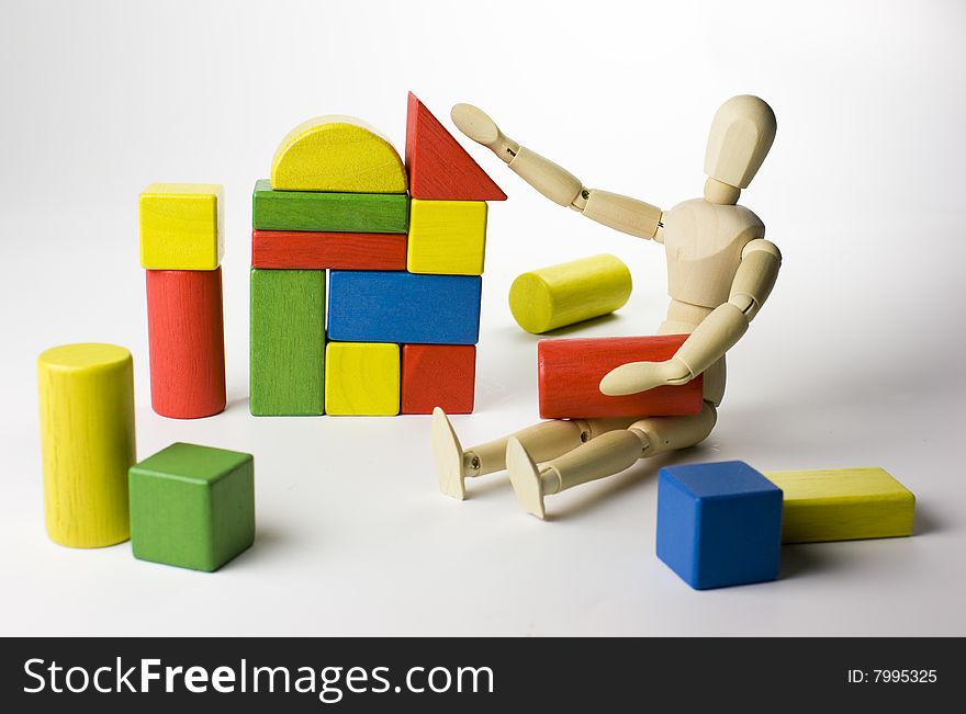 A wooden mannequin doll playing with colorful wooden toy blocks - cubes, building a house. A wooden mannequin doll playing with colorful wooden toy blocks - cubes, building a house.