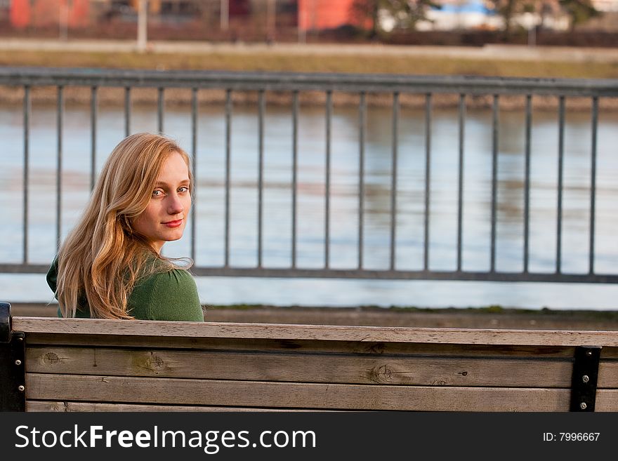 A female model sits on a bench by a river and looks back at the camera. A female model sits on a bench by a river and looks back at the camera.