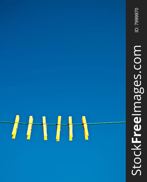 Yellow clothes pegs on a green washing line against a blue sky background.