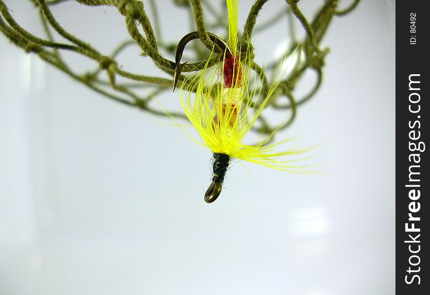 Macro of a yellow trout fly hanging from a fishing net. Macro of a yellow trout fly hanging from a fishing net.