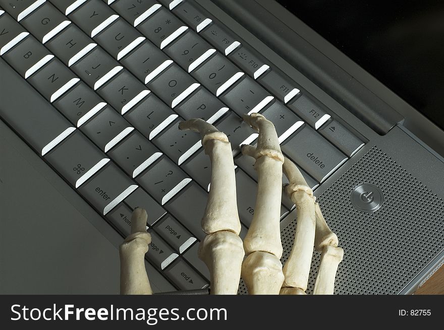 The boney hands of a skeleton type on a computer keyboard. The boney hands of a skeleton type on a computer keyboard