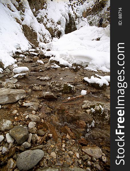 The banks of a river are frozen over as water trickles downstream over the rocky riverbed. The banks of a river are frozen over as water trickles downstream over the rocky riverbed.