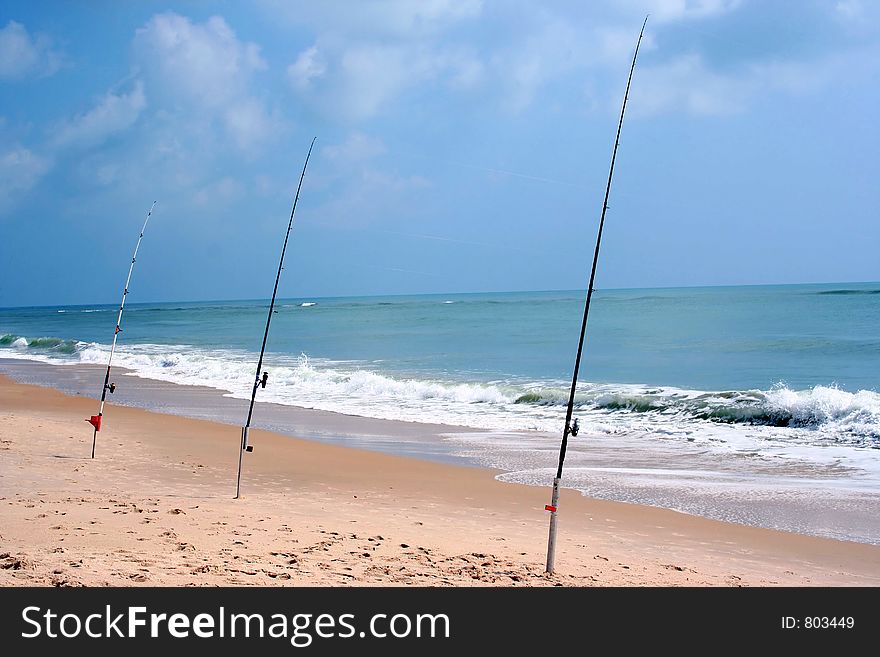 Three fishing poles sit at the beach waiting for a catch. Three fishing poles sit at the beach waiting for a catch
