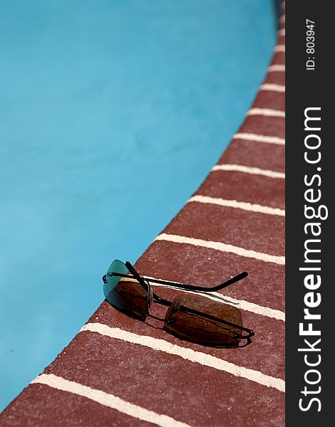 A pair of sun glasses by a pool. A pair of sun glasses by a pool