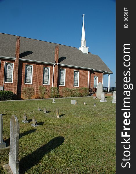 Brick church with stainglass windows, a steeple, and graveyard.