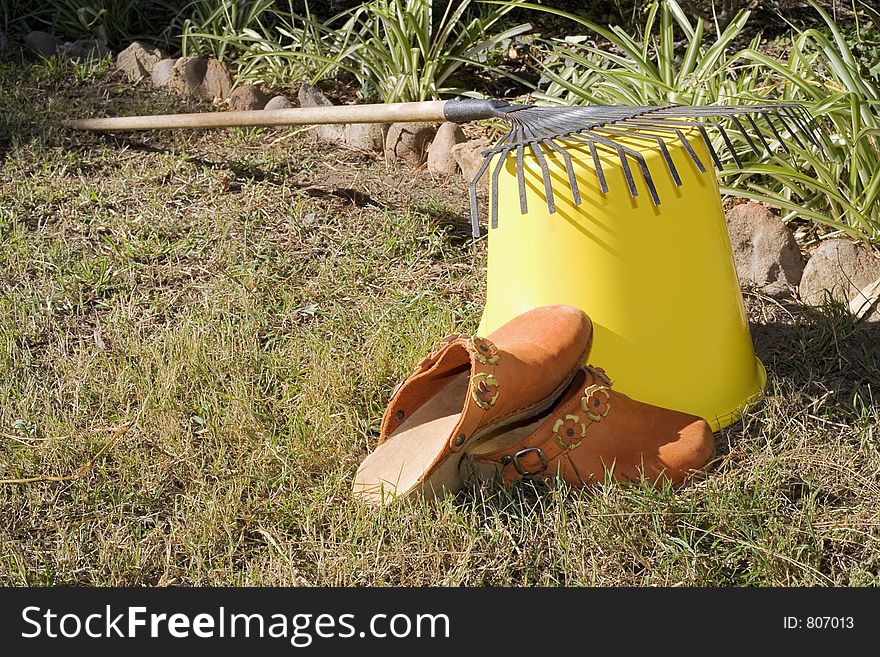 Rake resting on a bucket, and orange cloggs