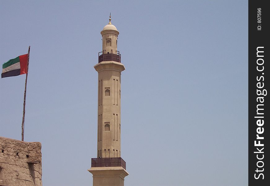 This is the spire on the Grand Mosque in Dubai. Dubai is in the United Arab Emirates. The United Arab Emirates flag is flying on the building next to it. This is the spire on the Grand Mosque in Dubai. Dubai is in the United Arab Emirates. The United Arab Emirates flag is flying on the building next to it.