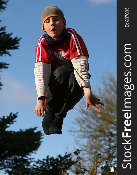 A young boy jumping on a trampolin, with a comical expression on his face. A young boy jumping on a trampolin, with a comical expression on his face