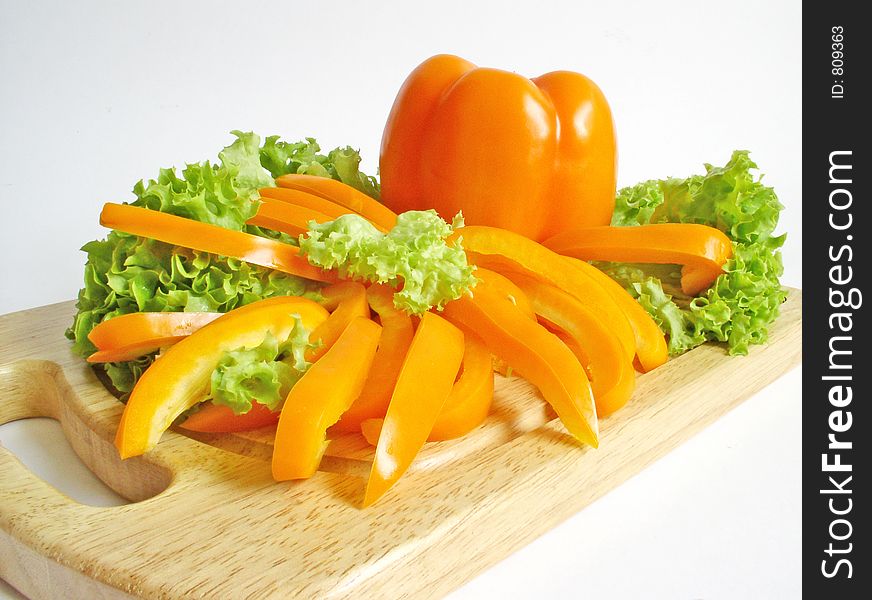 Orange paprika and lettuce on breadboard isolated