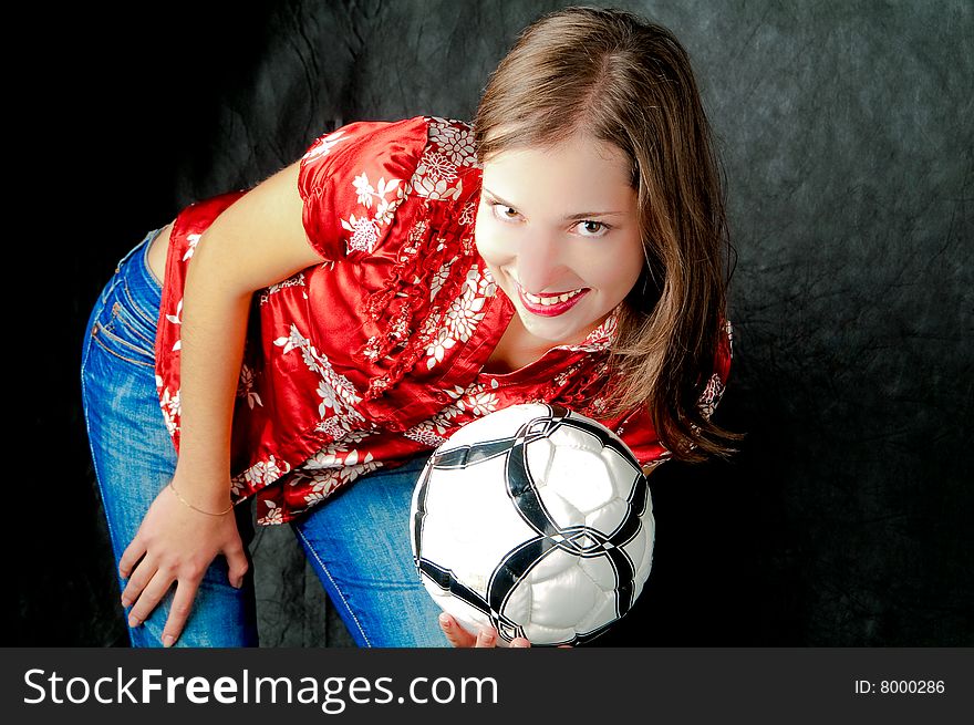 Young dark haired girl standing shaped with hand on hips holding ball and smiling on black background. Young dark haired girl standing shaped with hand on hips holding ball and smiling on black background