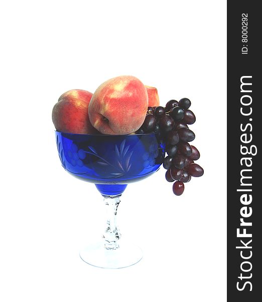 The peaches and red grape in the  blue  glass vase isolated. The peaches and red grape in the  blue  glass vase isolated
