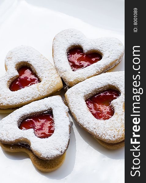 Heart shaped homemade jam cookies placed on a white plate with jam and a red background. Heart shaped homemade jam cookies placed on a white plate with jam and a red background
