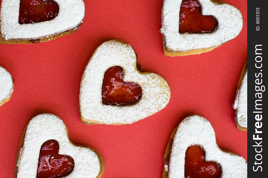 Heart shaped homemade jam cookies placed on a white plate with jam and a red background. Heart shaped homemade jam cookies placed on a white plate with jam and a red background