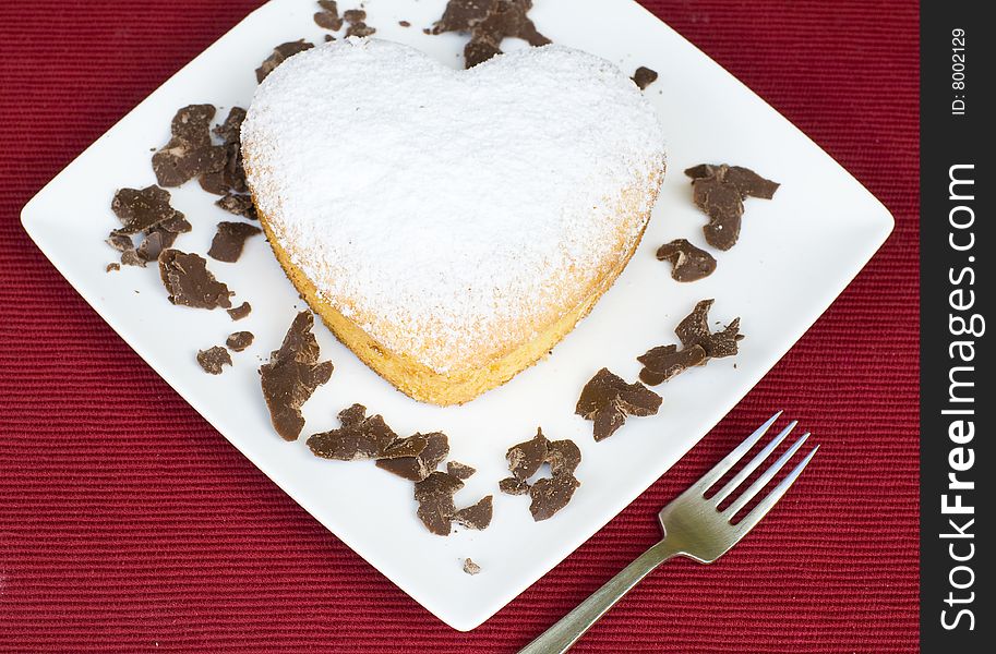 A heart shaped cake presented on a white plate with chocolate garnish. A heart shaped cake presented on a white plate with chocolate garnish