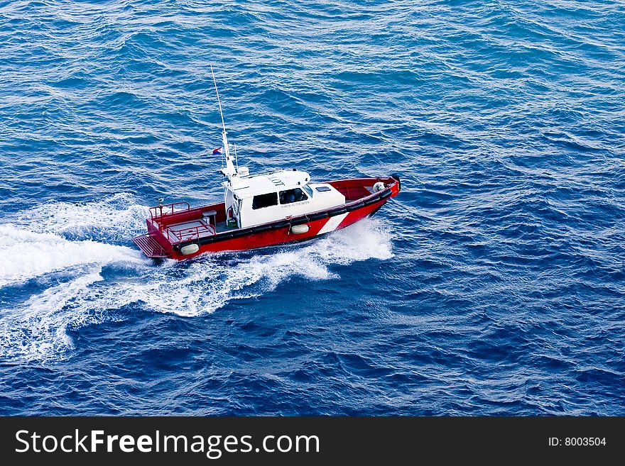 A red and white pilot boat churning through the water of a bay