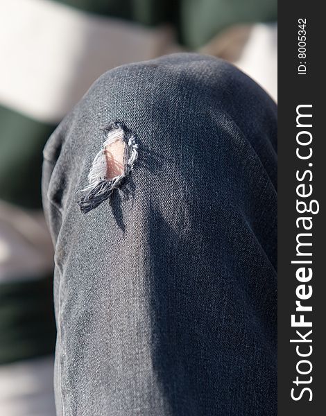 A male model sits on a curb while modeling his old jeans with a hole in them. A male model sits on a curb while modeling his old jeans with a hole in them.