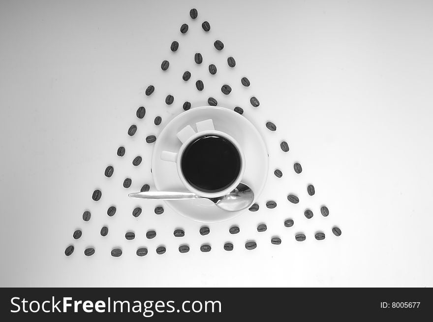 Triangle made of coffee grains with the cup of coffee on the saucer at the center. Triangle made of coffee grains with the cup of coffee on the saucer at the center.