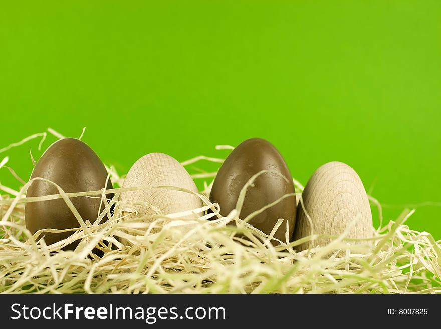 Chocolate and wooden easter eggs in a nest, arranged in a row, green background.