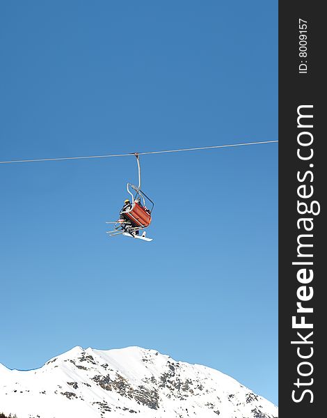 Skiers are riding in chairlift in a ski area, low angle view, Italy. Large copy-space at the top.