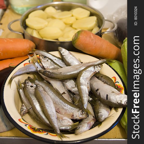 Many silver raw fish on yellow plate with orange carrot end green aubergine