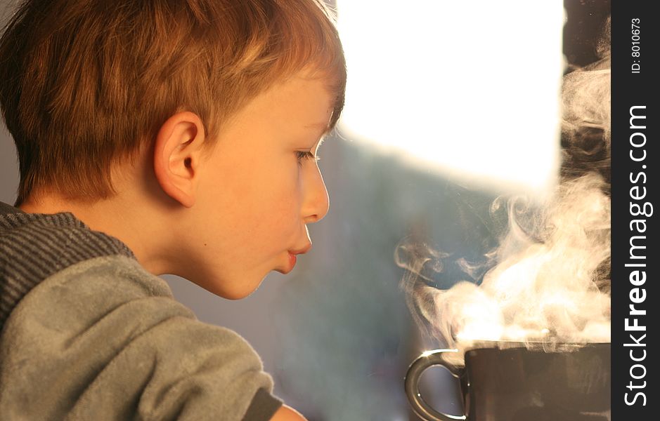 Cute young boy carefully blowing at a huge mug of hot tea