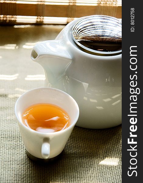 A picture of a cup of tea and a teapot basking under the sun. A picture of a cup of tea and a teapot basking under the sun
