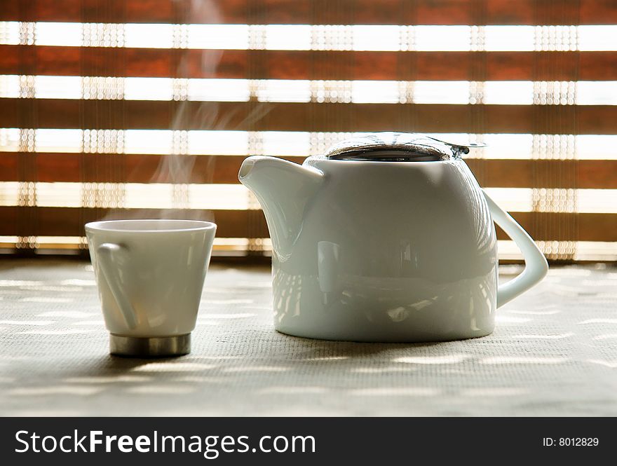 A picture of a cup and teapot against a bamboo curtain. A picture of a cup and teapot against a bamboo curtain