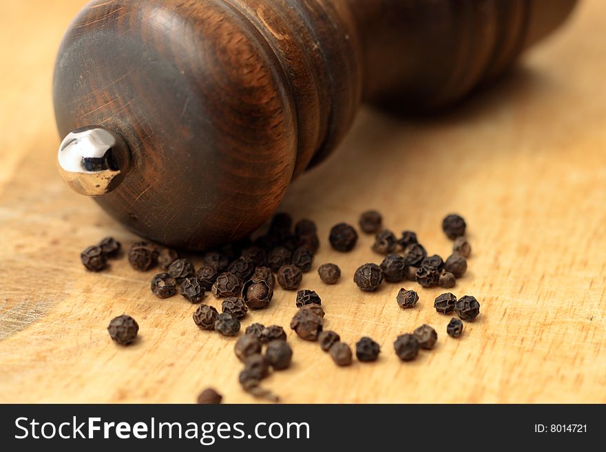 Close-up of black pepper and old pepper-mill lying on wooden background. Close-up of black pepper and old pepper-mill lying on wooden background