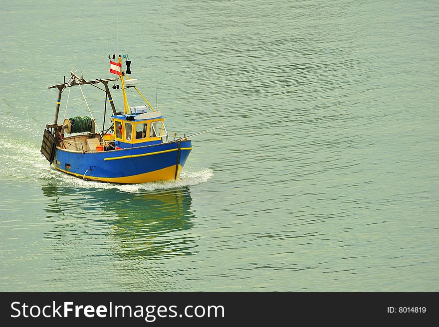 A small fishing boat coming into harbour. Space for text on the water.