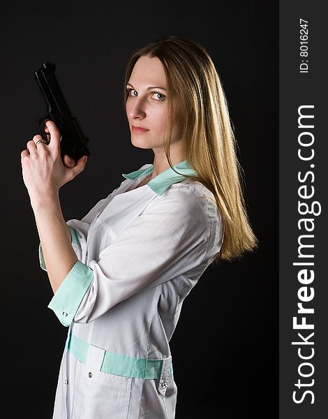 Girl in a doctor's smock with gun on a dark background. Girl in a doctor's smock with gun on a dark background