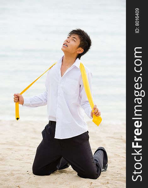 A young business man on his knees at the beach