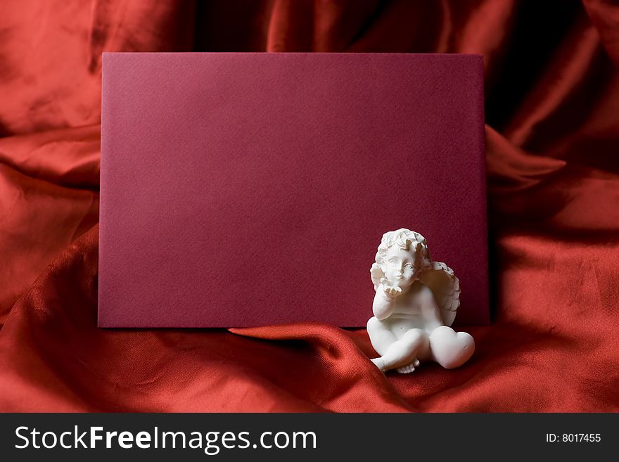 A red valentine card - letter on red satin fabric background with a little white angel sending a kiss to the message recipient.
