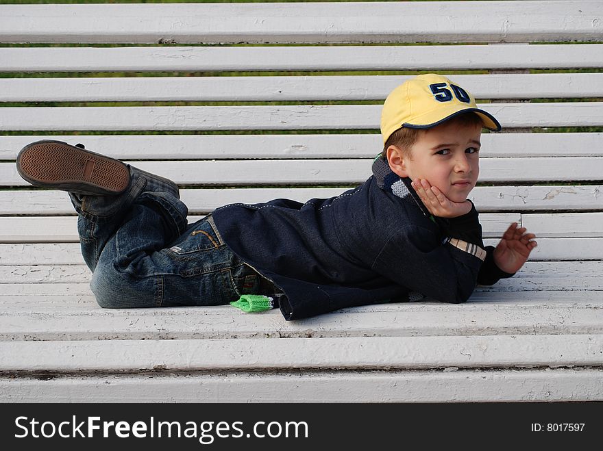 Young boy sitting on a bench in a park. Young boy sitting on a bench in a park.