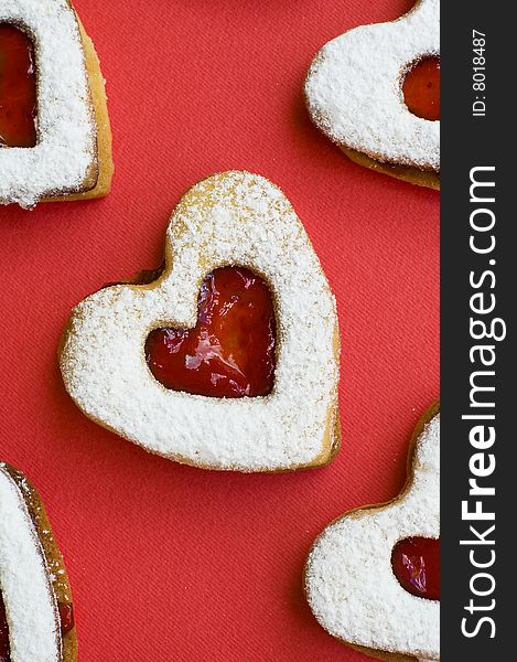 Heart shaped homemade jam cookies placed on a white plate with jam and a red background. Heart shaped homemade jam cookies placed on a white plate with jam and a red background