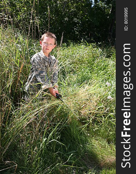 Boy in American Army camoflauge hiding in the grass and scowling