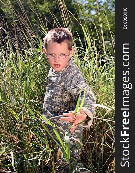Young boy in camoflauge hiding in the grass