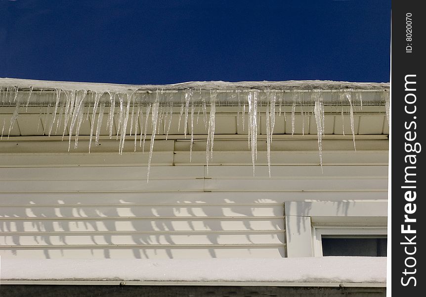 A row of icicles in a garage roof against a deep blue sky.