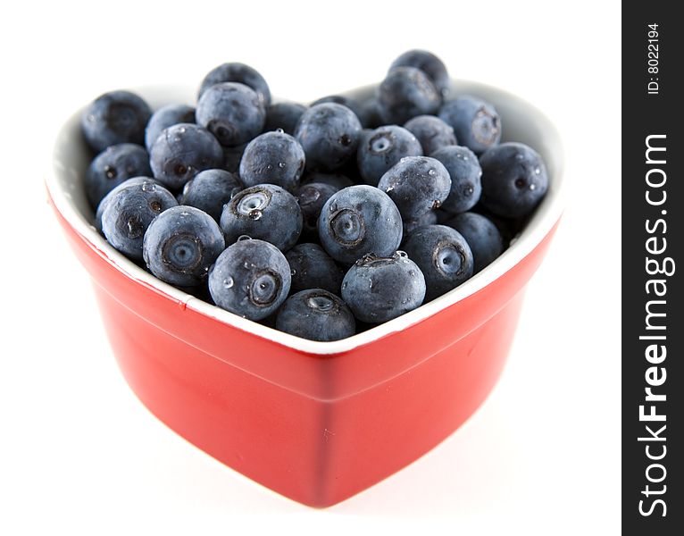 Heart shaped bowl of fresh blueberries with shallow depth of field and white background. Heart shaped bowl of fresh blueberries with shallow depth of field and white background