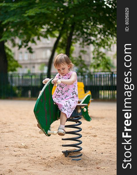 Small thoughtful beauty girl on spring fish swing. Hot summer. Small thoughtful beauty girl on spring fish swing. Hot summer.